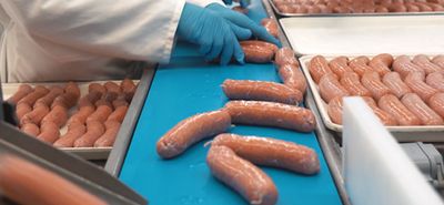 Worker handling sausages on a food processing conveyor belt.