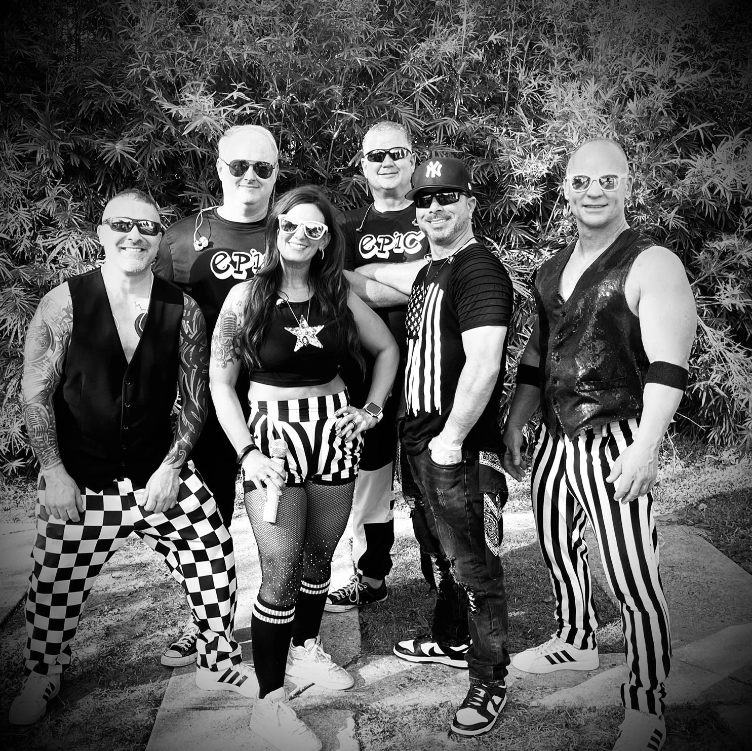 Black and white photo of a stylish band posing outdoors with patterned pants and sunglasses.