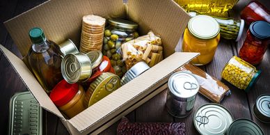 A cardboard box filled with various canned and jarred food items.