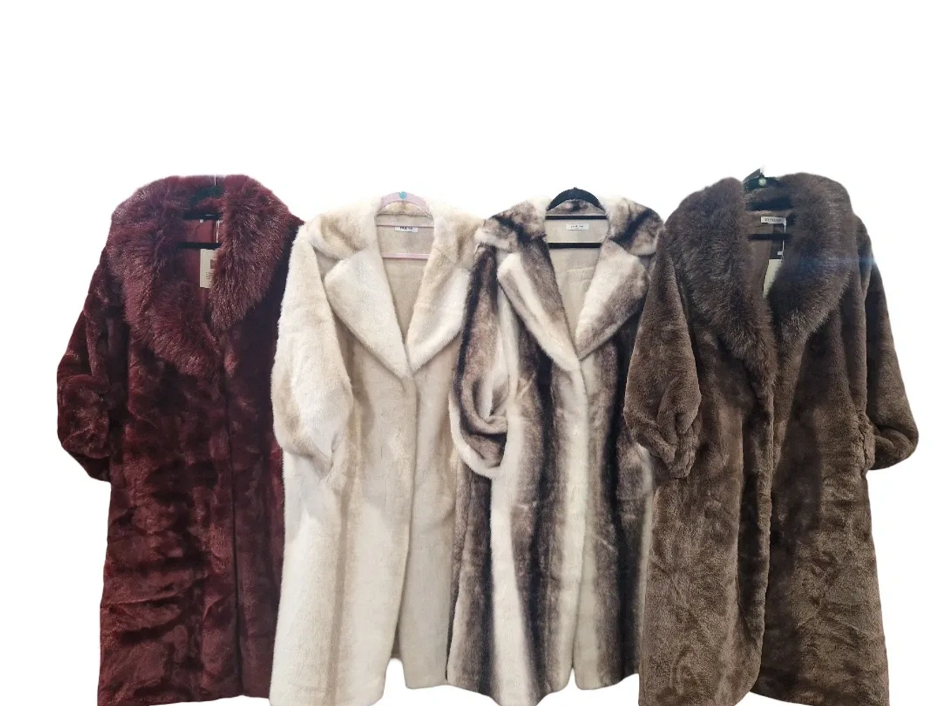 Four luxurious fur coats in various colors hanging on hangers.