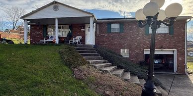 A brick house with a porch, stairs, and a vintage street lamp in the front yard.