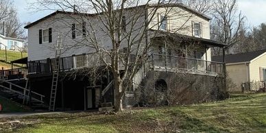 A two-story house with a wraparound porch and bare trees in front.