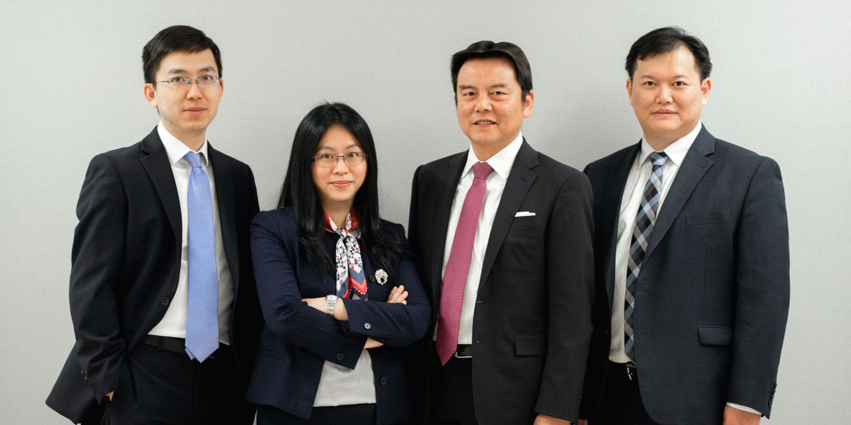 Four professionals dressed in business attire posing against a plain background.