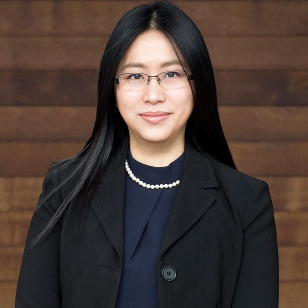 Professional woman with glasses and pearl necklace in black blazer.