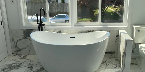Modern white freestanding bathtub by large window.