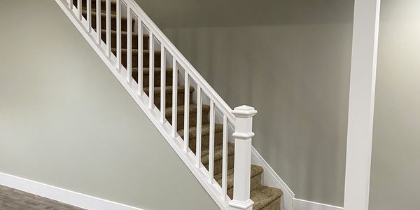 Carpeted staircase with white railing against gray wall.