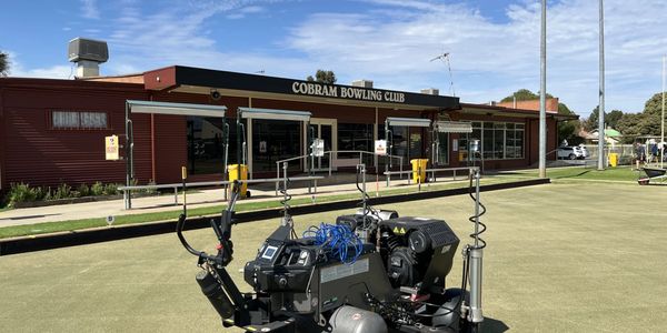 A bowling green with a robot machine and Cobram Bowling Club building in the background.