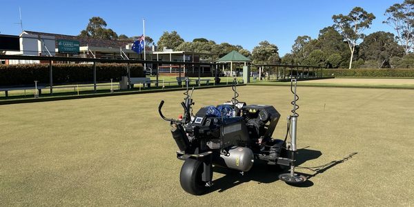 A robotic lawn mower on a bowling green under clear skies.