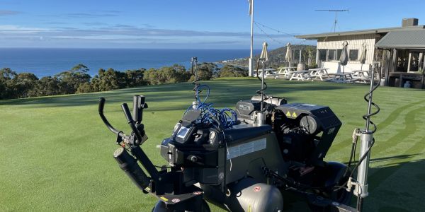 Automated golf course maintenance robot on a green with ocean view.
