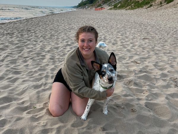A woman kneeling on the beach hugging her dog with a smile.