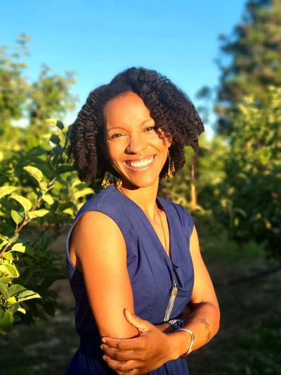 Smiling woman in blue dress outdoors with braided hair.