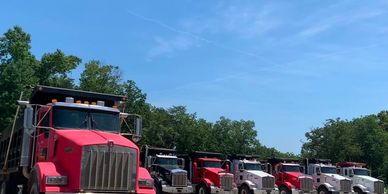 A lineup of several dump trucks parked outdoors under a clear blue sky.