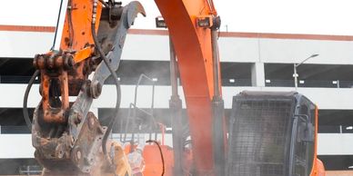 Excavator working on demolition with dust clouds around.