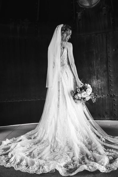 Bride in a long lace wedding gown holding a bouquet, standing gracefully.