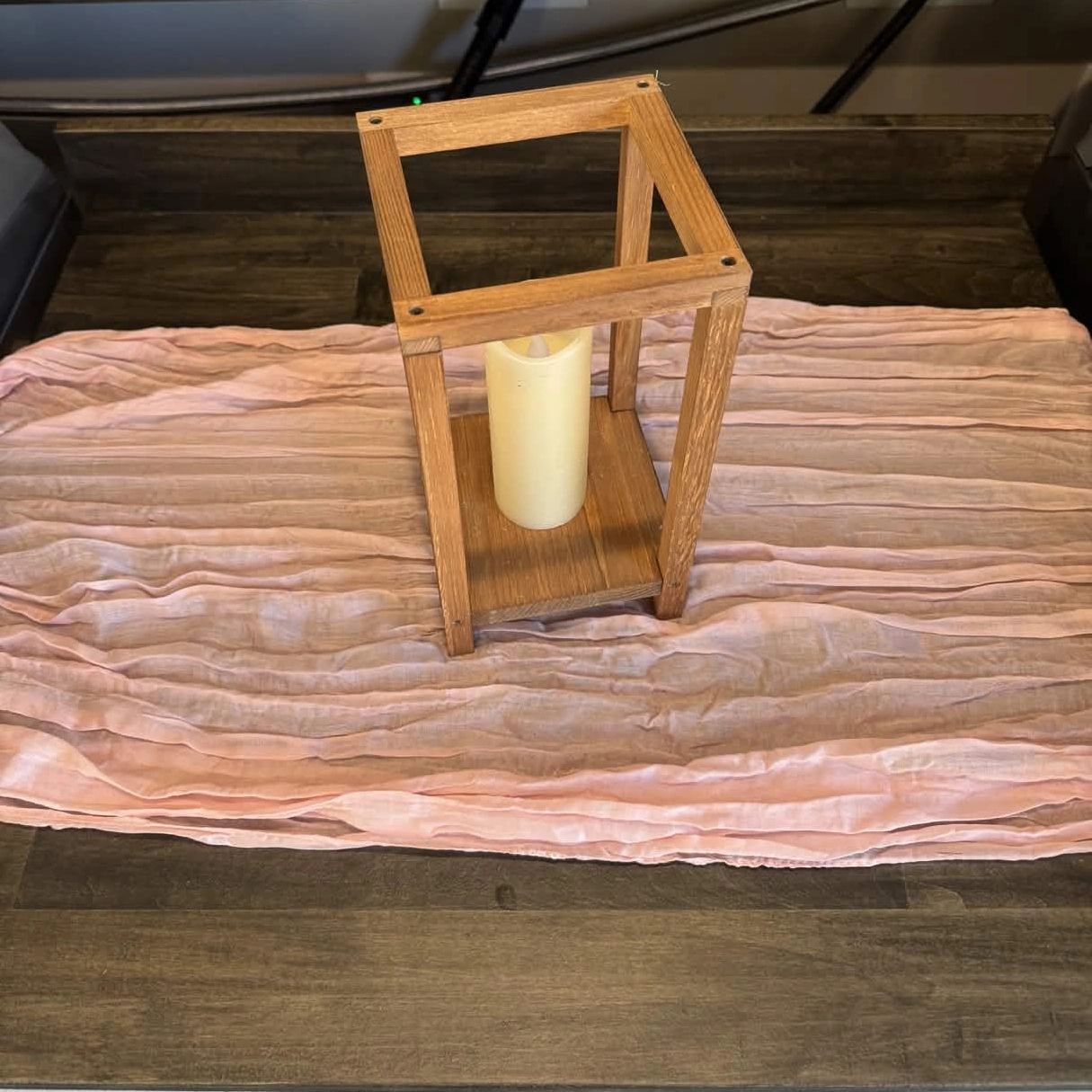 Wooden candle holder with a white candle on a pink cloth on a wooden table.