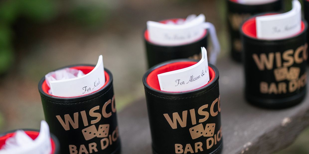 Black Wisconsin Bar Dice cups with folded papers inside, placed on a wooden surface.