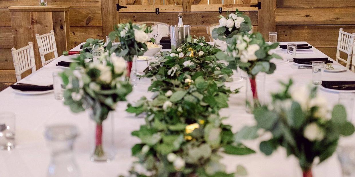 Elegant table centerpiece with green foliage and white flowers in a rustic wooden setting.