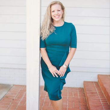 Woman in teal dress leaning against a white pillar, smiling.