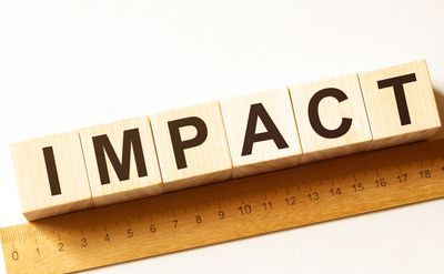 Wooden blocks with letters spelling the word impact and a ruler underneath.