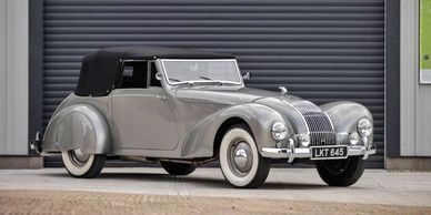 Classic silver convertible car parked in front of a black garage door.