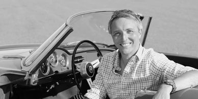 Smiling man sitting in a vintage convertible car.