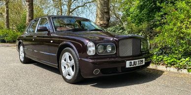A classic dark purple Bentley parked on a sunny road.