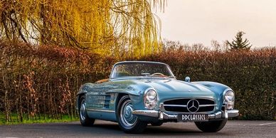 Classic blue Mercedes-Benz convertible parked outdoors with autumn foliage.