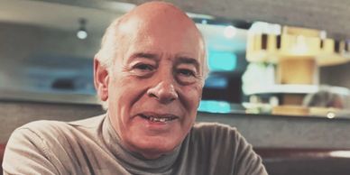 Elderly man smiling warmly in a cozy indoor setting.