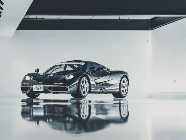 A sleek black sports car with reflective floor in a minimalist garage.