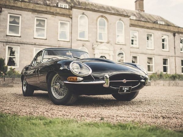 Classic black Jaguar E-Type parked in front of an elegant historic building.
