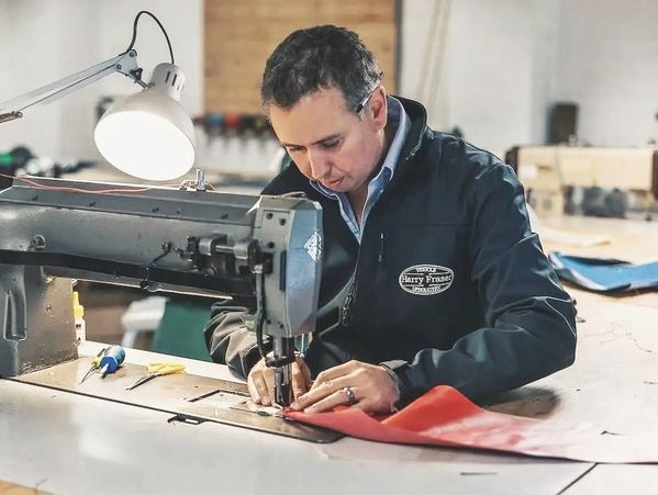 A man operates a sewing machine, stitching red fabric in a workshop.