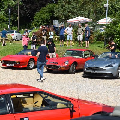 A gathering of classic and modern sports cars with people admiring them outdoors.