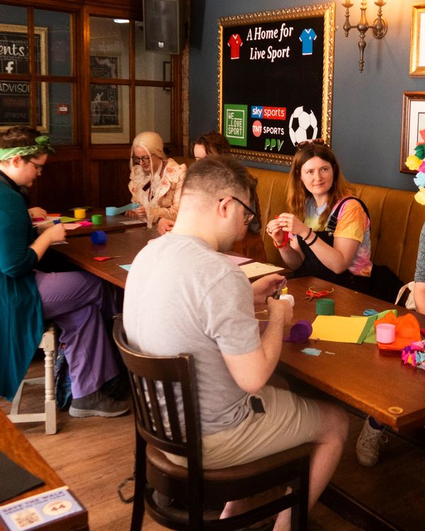 People crafting colorful decorations at a wooden table in a cozy room.