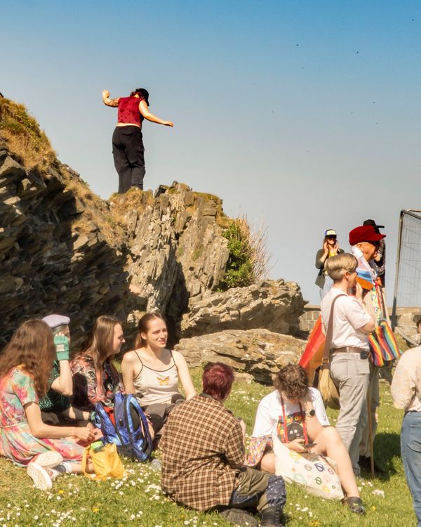 Group of people enjoying a sunny day near rocky cliffs and grassy area.