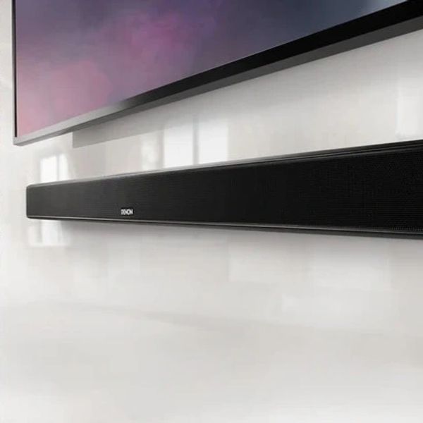 A sleek black soundbar mounted on a white wall below a TV.