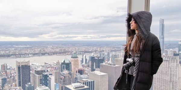 Woman in winter coat overlooking a city skyline from a high vantage point.