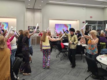 Group of people dancing indoors with foam sticks.