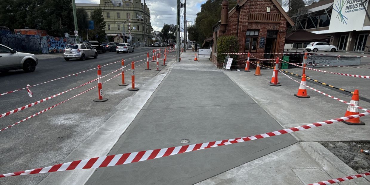 Newly paved sidewalk blocked off by safety cones and tape.