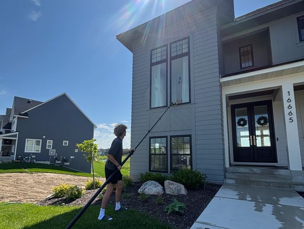 Person cleaning second-story window with an extended pole on a sunny day.