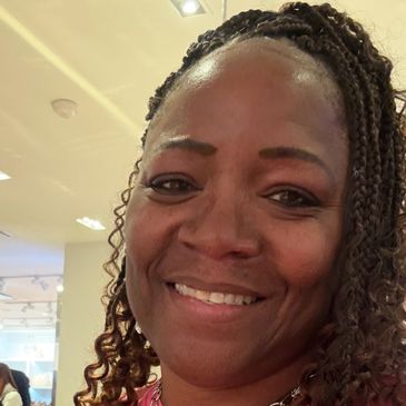 Smiling woman with braided hair in a well-lit indoor space.