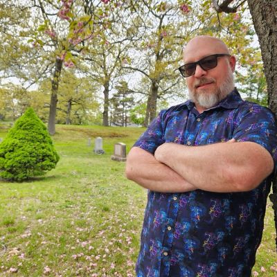 Man with sunglasses standing in a cemetery.