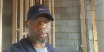 Man wearing a black cap indoors with unfinished brick wall.