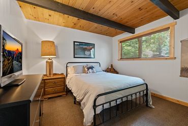 Cozy bedroom with wooden ceiling and natural light from the window.