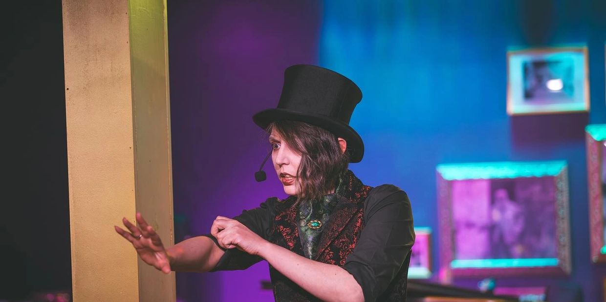 A performer in a top hat gestures dramatically on stage.