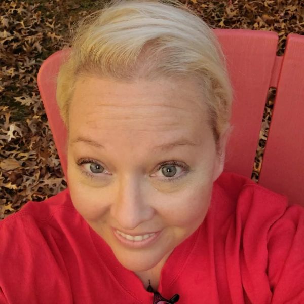 Smiling woman in a red top sitting outdoors on a red chair.