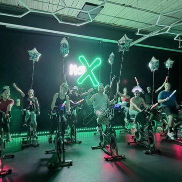 Group of people enjoying a neon-lit spin class with balloons and glow sticks.