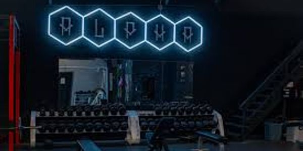 Dimly lit gym with neon 'RLDHA' sign above weights.