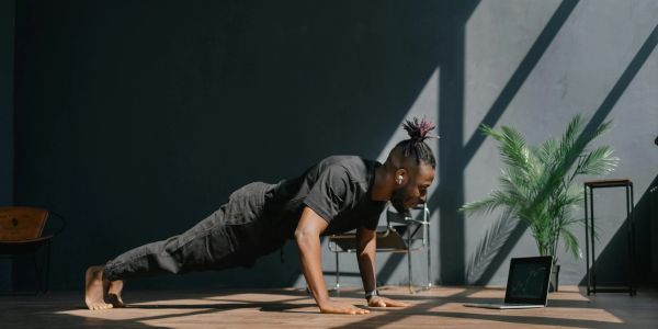Man doing push-ups indoors with sunlight and a laptop nearby.