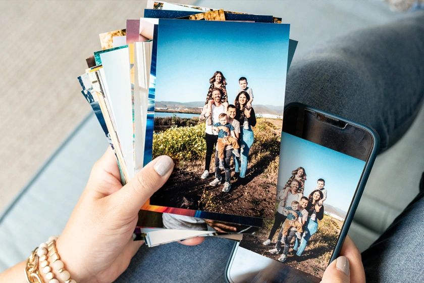 Hand holding printed family photos with a scenic outdoor background.