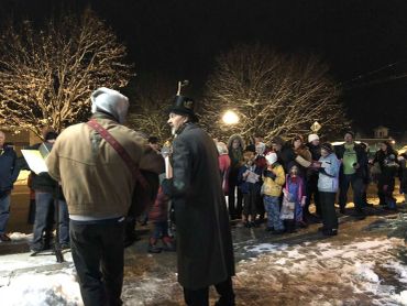 A group caroling outdoors at night in winter clothing.